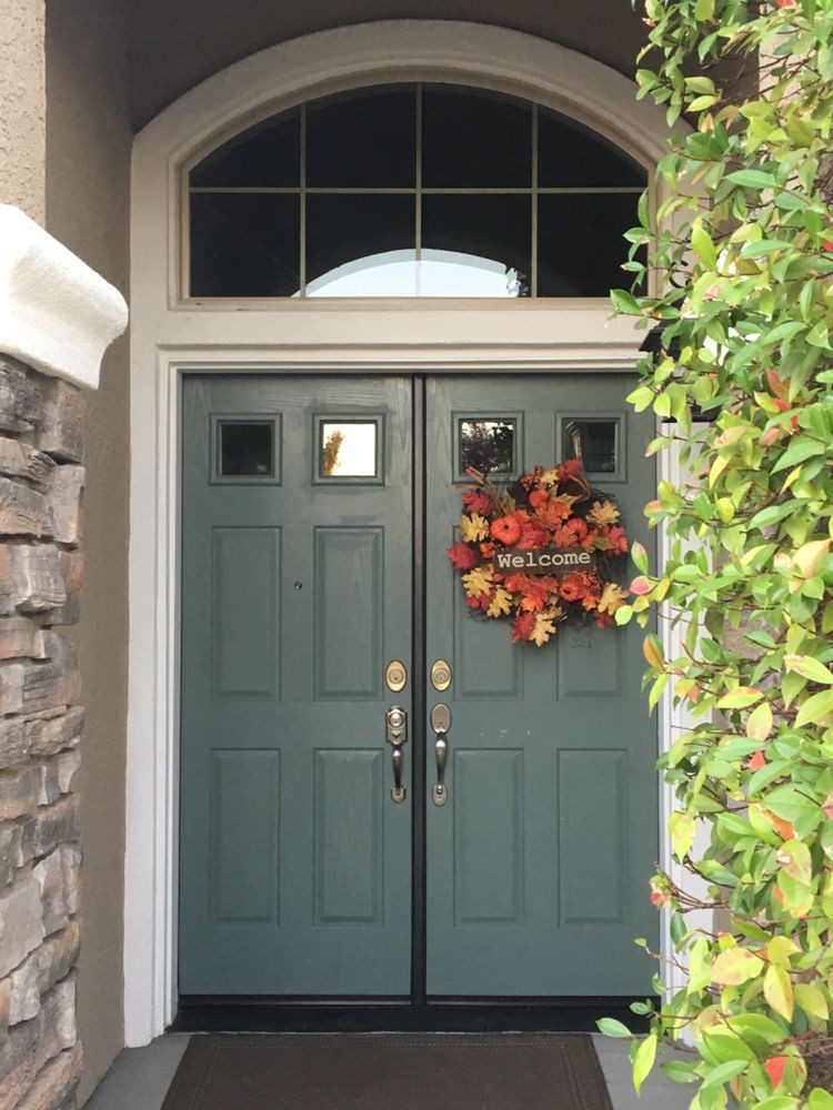 A front door decorated with an autumn wreath and surrounded by greenery.