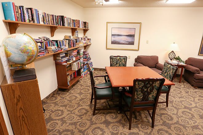 A cozy library room with bookshelves, a table with chairs, and a sofa.