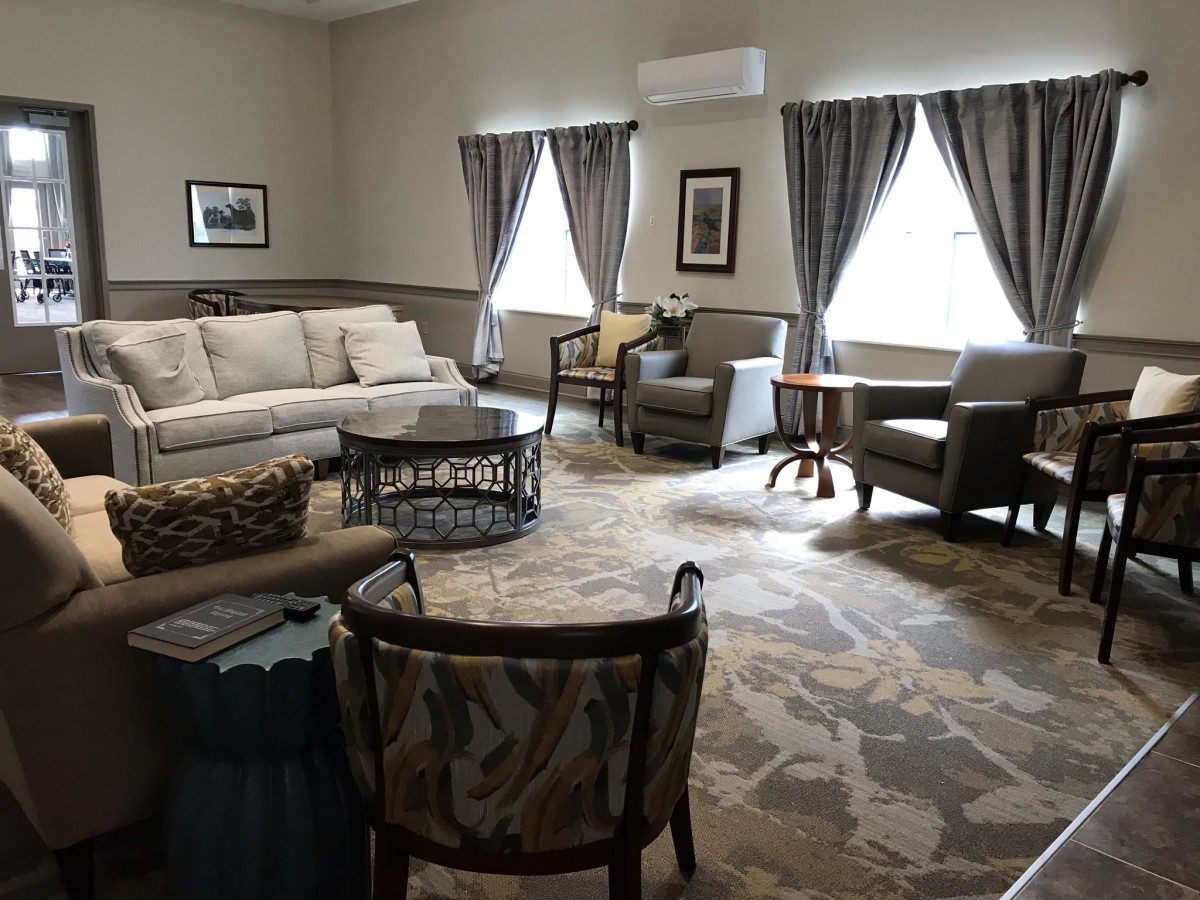 A cozy living room with a sofa, several chairs, and a coffee table, featuring elegant curtains and wall art.