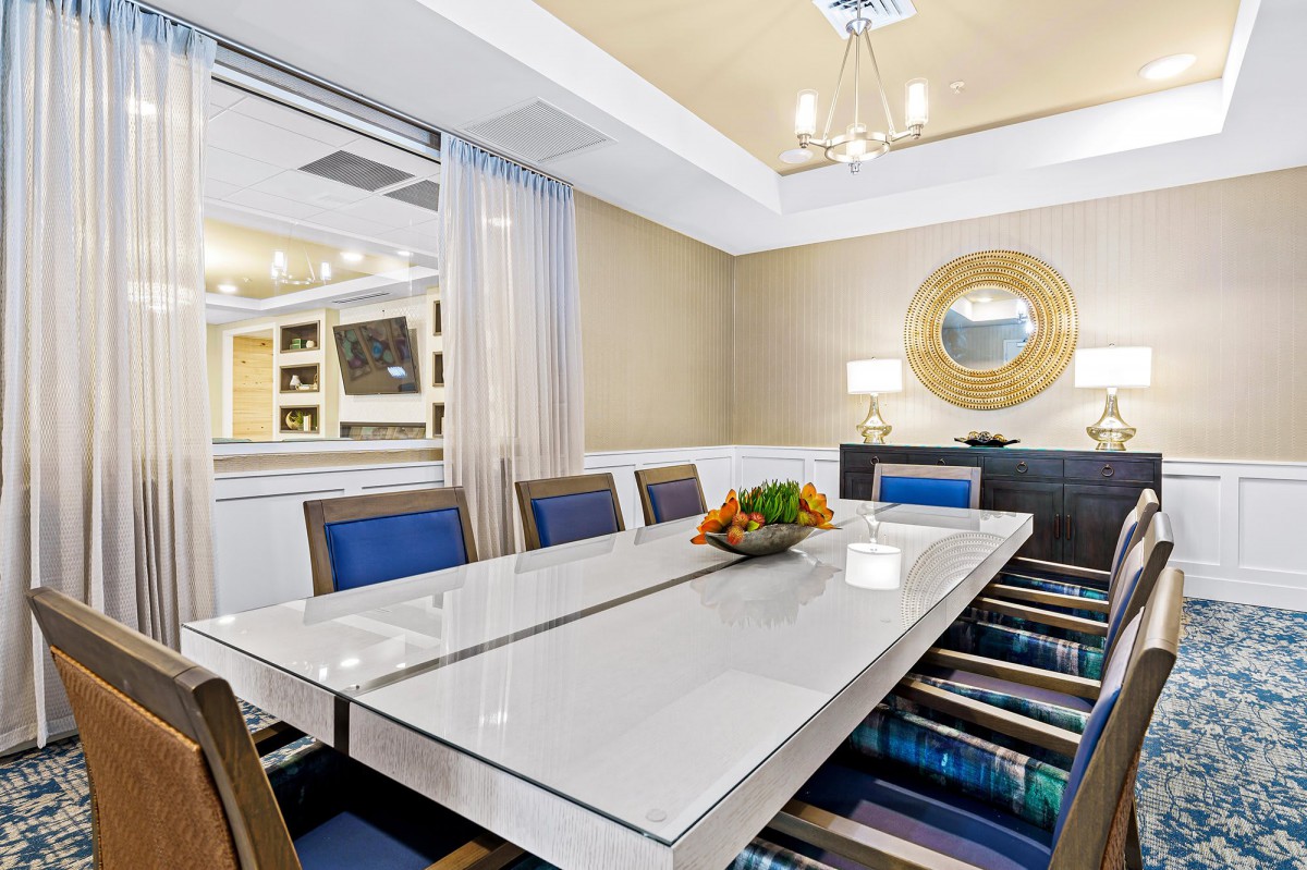 A modern and elegant dining room featuring a reflective table, stylish chairs, a decorative mirror, and a chandelier.