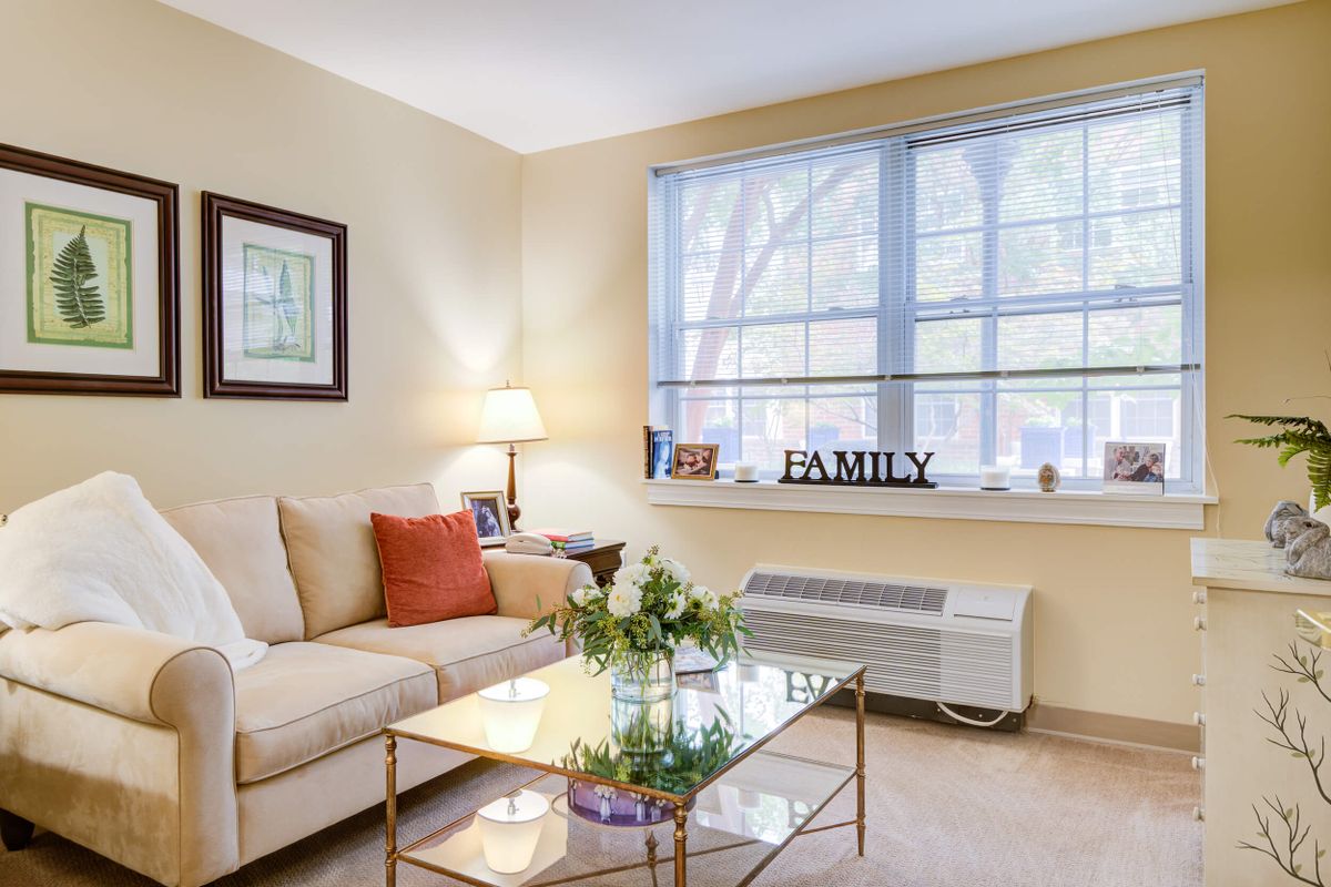 A cozy living room with a beige sofa, glass coffee table, and decorative elements including a family sign by the window.