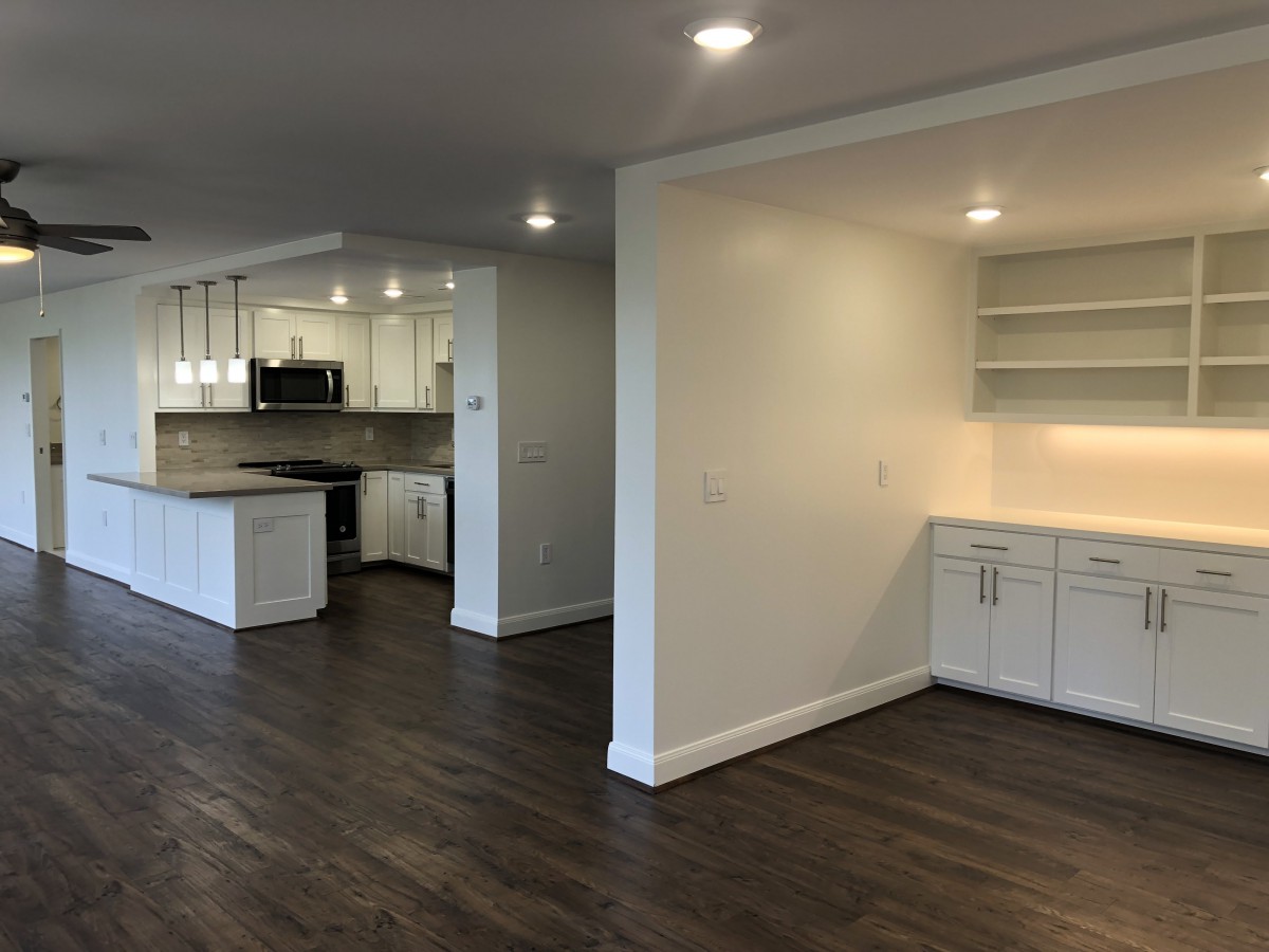 A modern open-concept kitchen and dining area with wood flooring and white cabinetry.