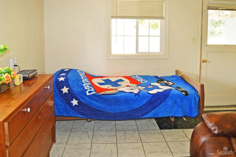 A simple bedroom with a bed covered by a blue blanket featuring cartoon characters.
