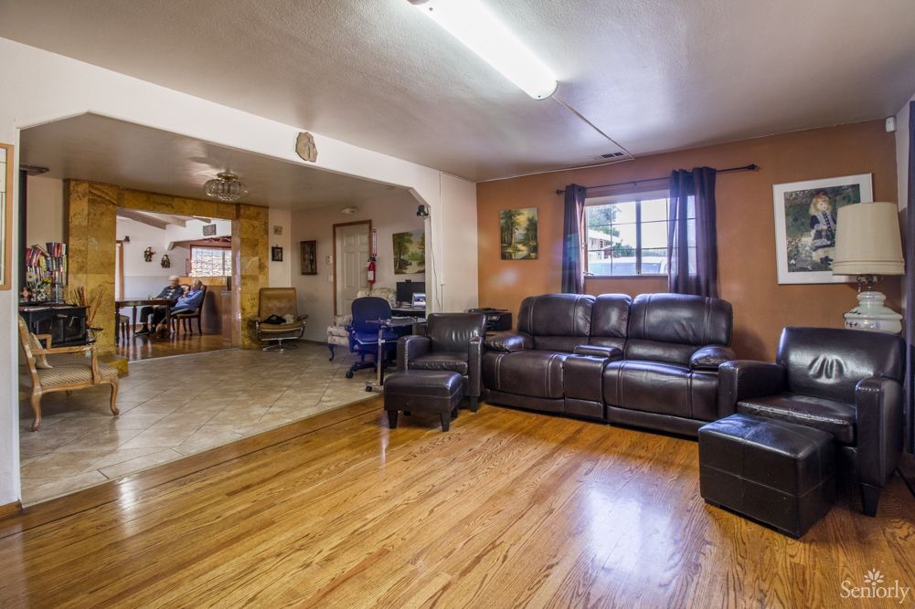 A cozy living room with a leather sofa and hardwood floors, featuring an open layout leading into the kitchen area.