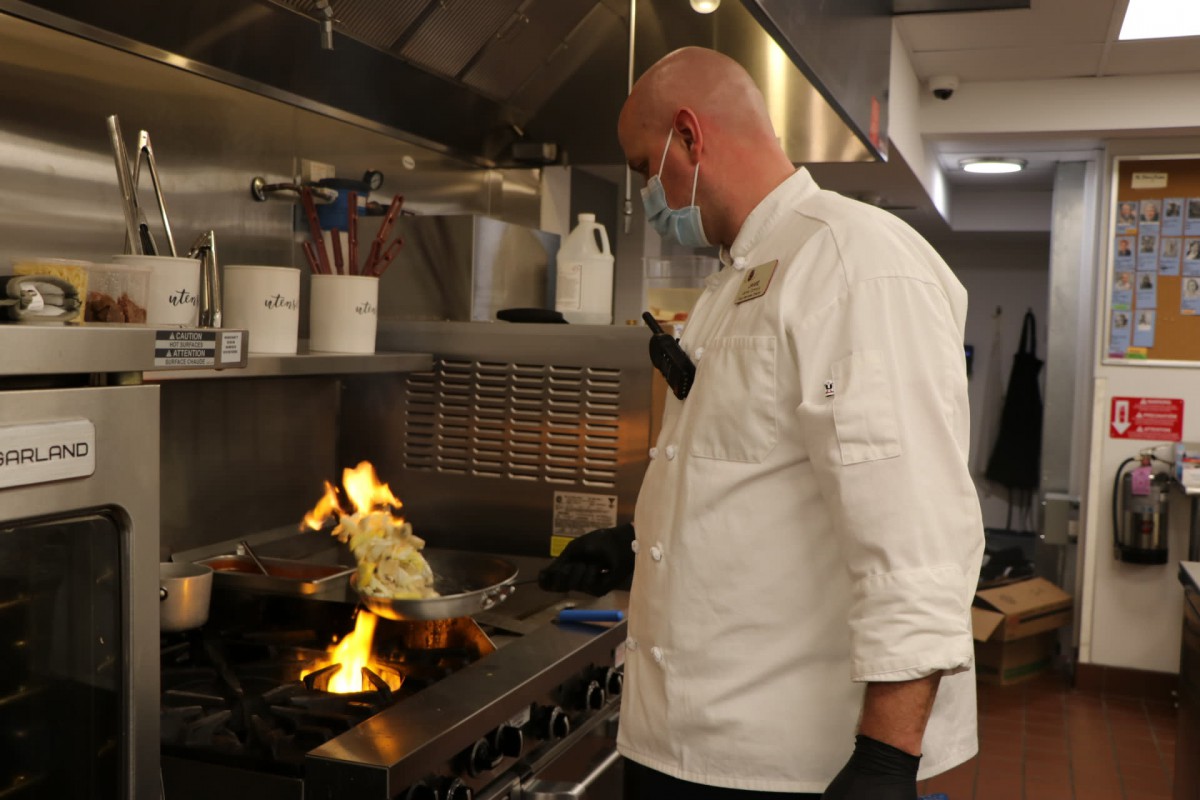 A chef skillfully cooks in a professional kitchen with a high flame on the stove.