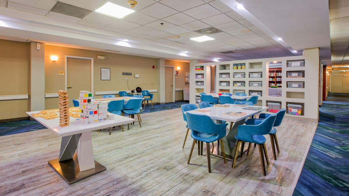 A modern library reading area with tables, blue chairs, and bookshelves filled with books.