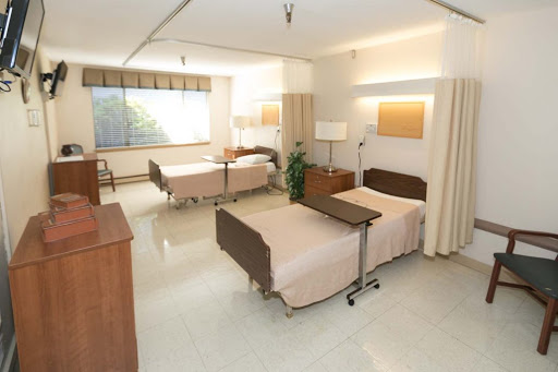 A well-lit and spacious hospital patient room with two beds and modern furnishings.