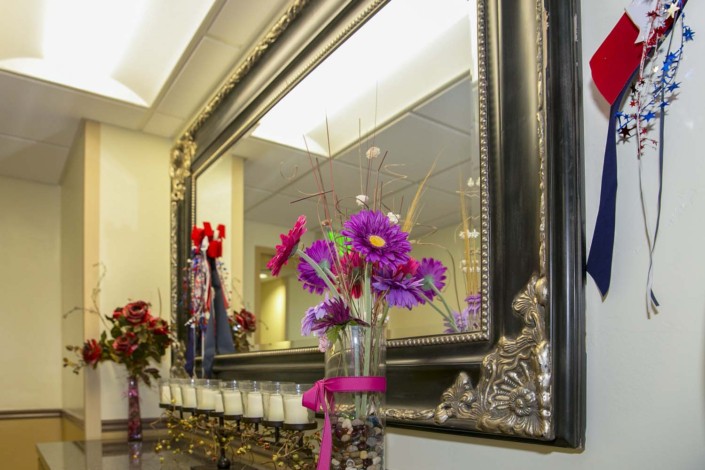 A decorative interior scene with a large ornate mirror, colorful flowers in a vase, and candles.