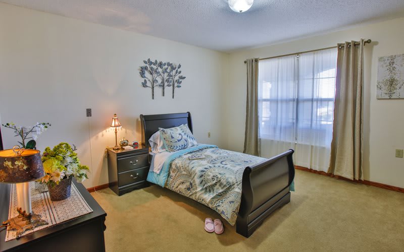 A cozy bedroom with a single bed and a nightstand, softly lit by a lamp.