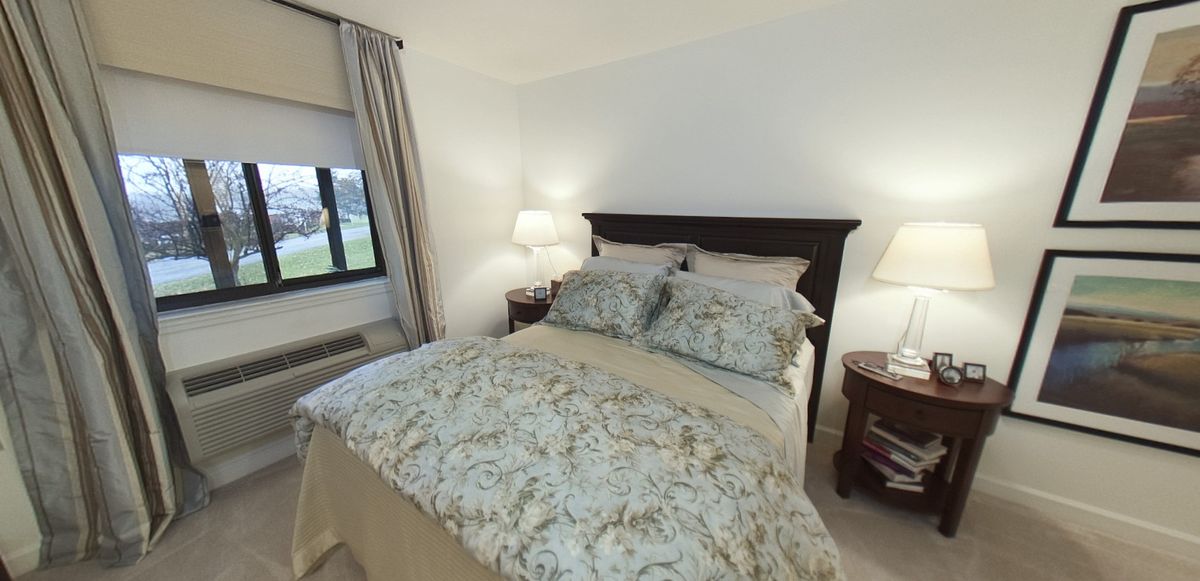 A cozy bedroom with a neatly made bed, adorned with floral patterned pillows and bedding. Two lamps on nightstands flank the bed, adding warmth to the room.