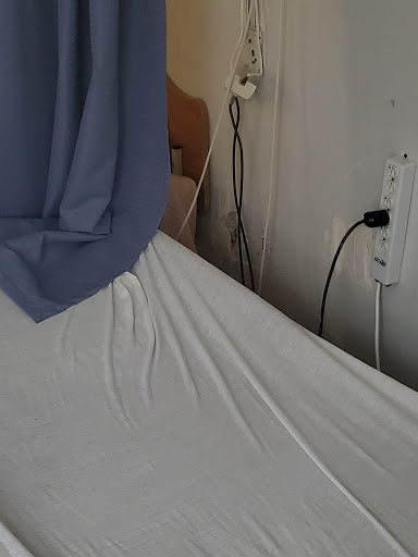 A hospital bed with a sheet and curtain, showing an electrical outlet in the background.