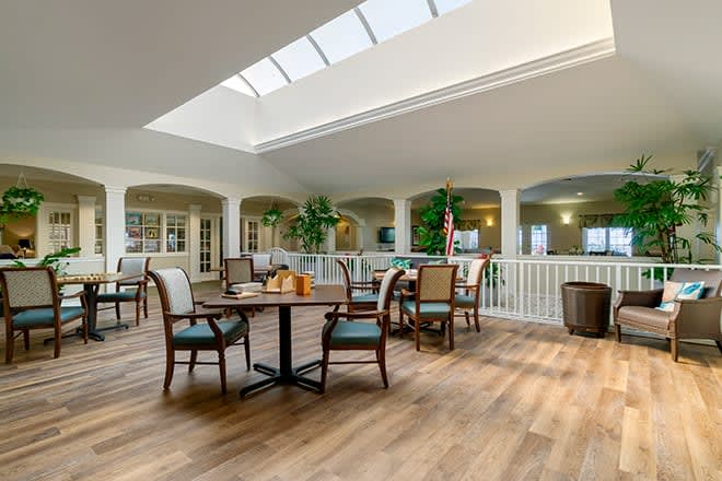 A bright and open dining area with tables and chairs under a skylight, featuring indoor plants and wood flooring.