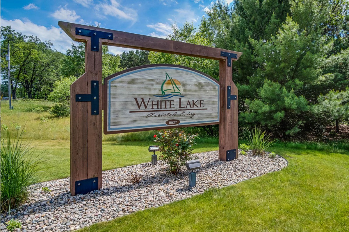 A wooden entrance sign for White Lake, surrounded by greenery.
