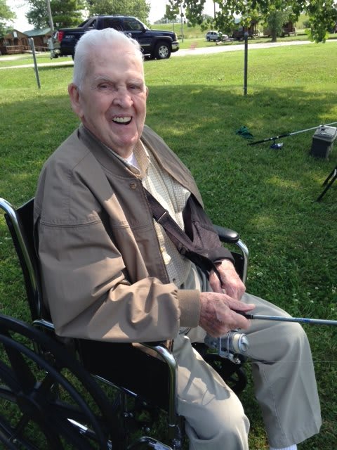 Elderly man smiling while fishing in a wheelchair outdoors.