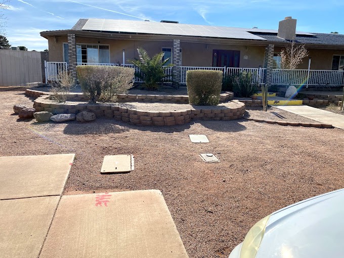 A single-story house with a desert landscaped front yard featuring bushes and pavement.