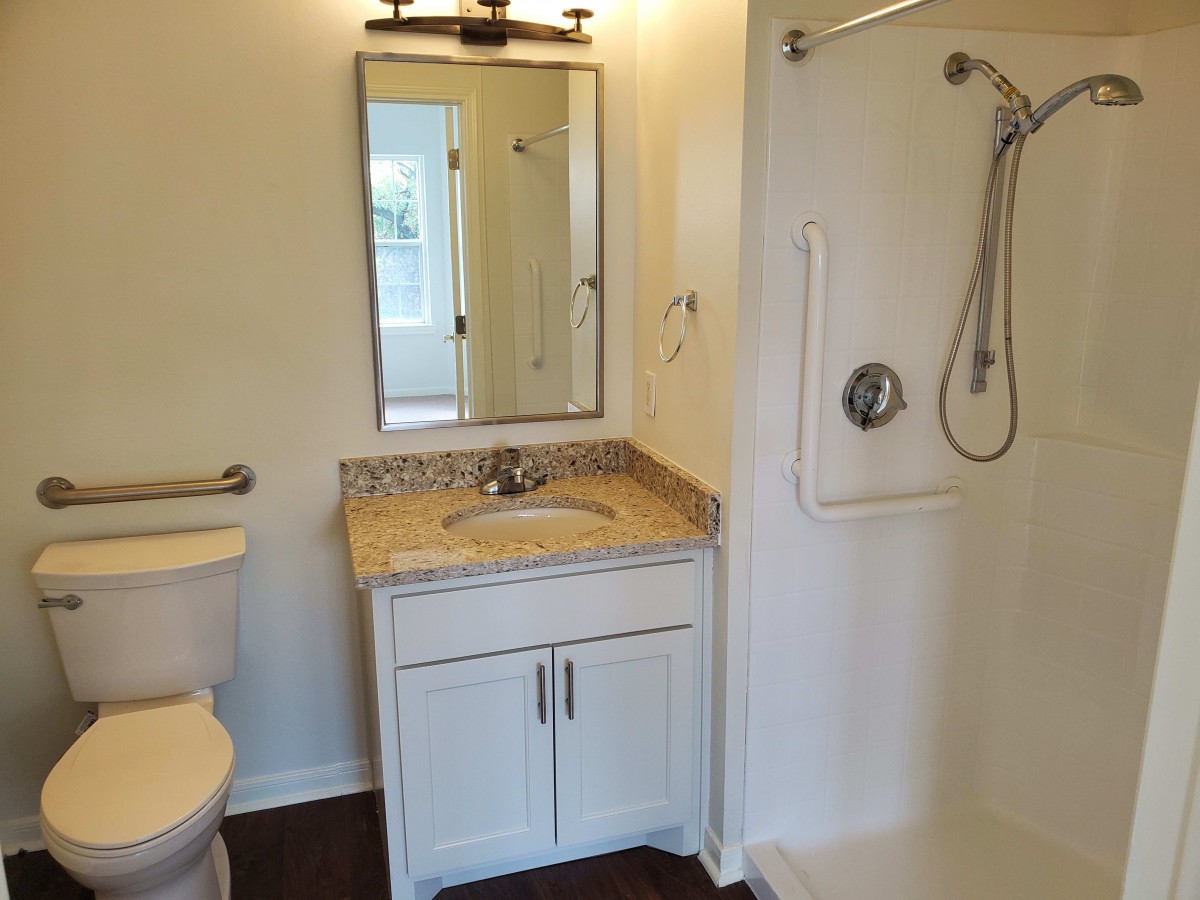 A well-lit bathroom featuring a shower, vanity with sink and mirror, and a toilet.