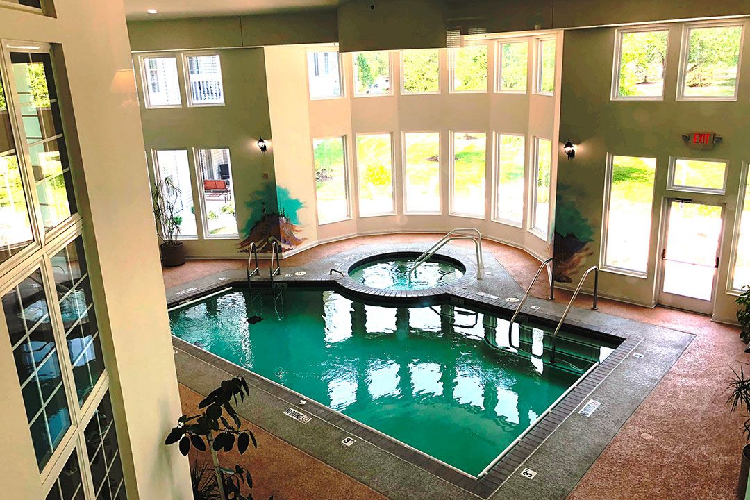 A well-lit indoor swimming pool with a jacuzzi and large windows letting in natural light.