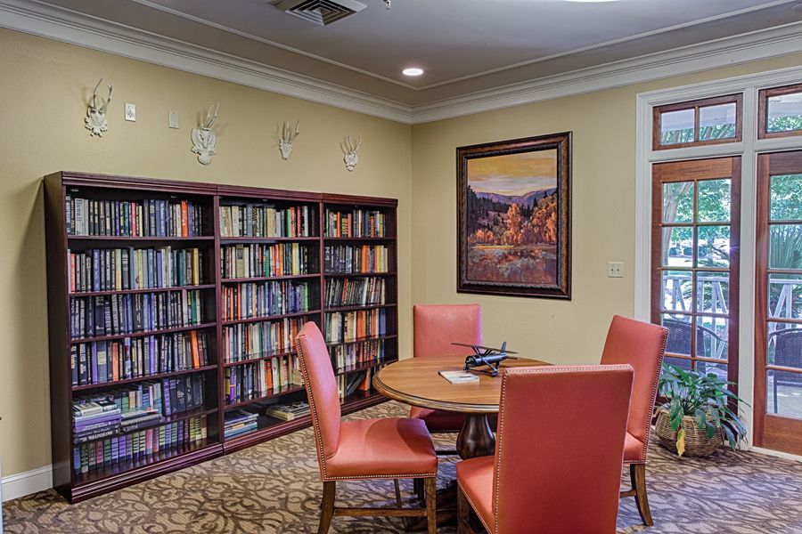 A cozy library room with bookshelves, a round table, and orange chairs.