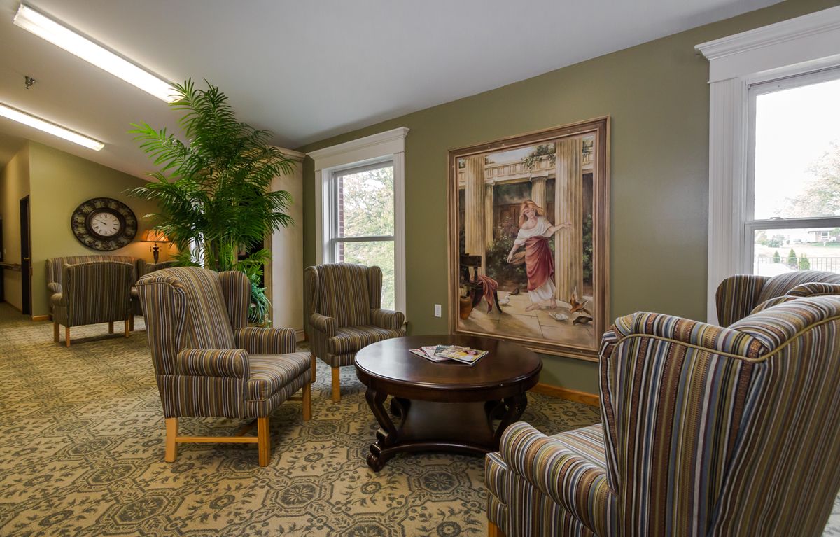 A cozy living room with four striped armchairs, a central wooden coffee table, a large painting on the wall, and a decorative plant by the window.