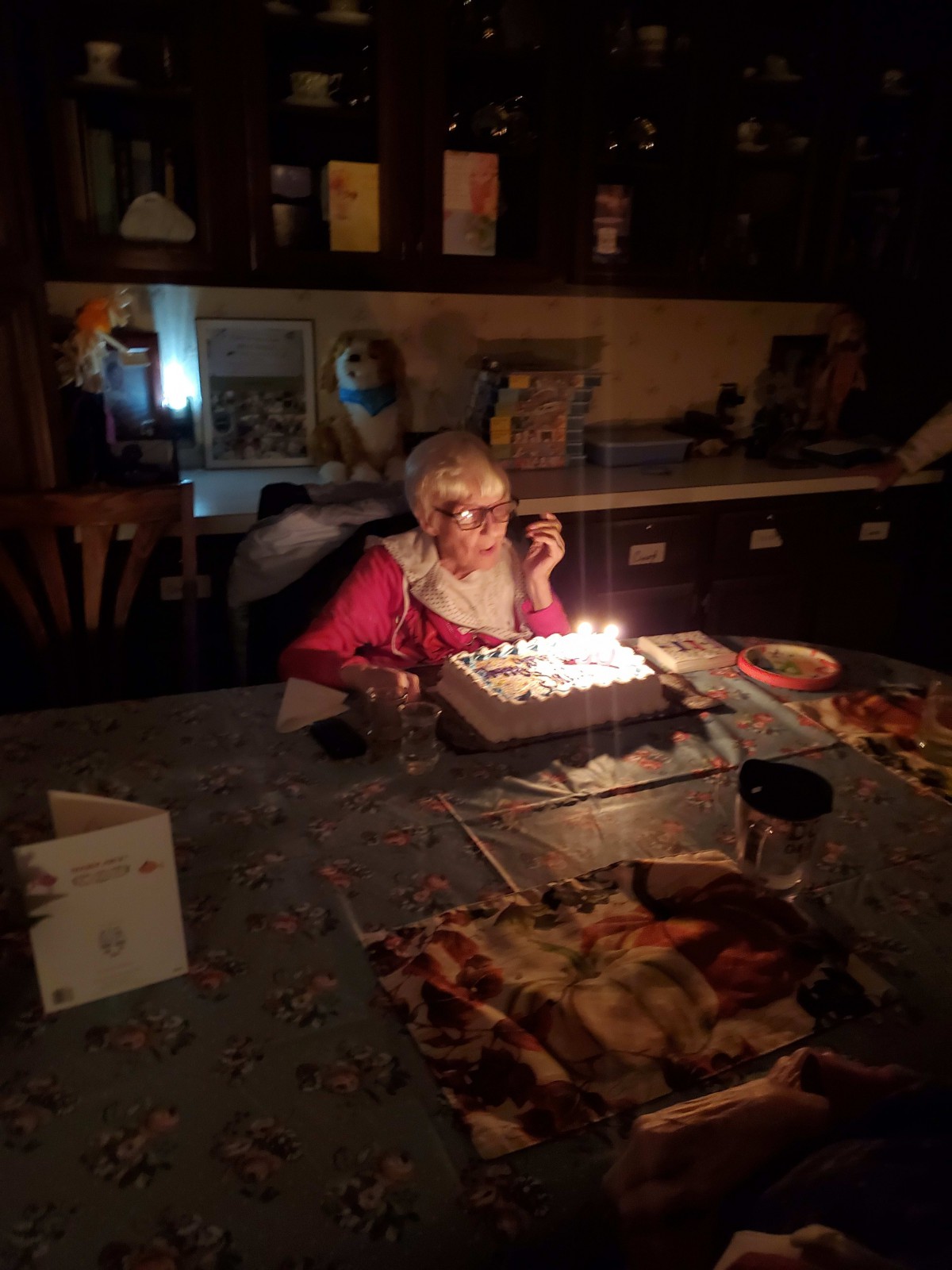 An elderly person celebrating a birthday with a cake lit by candles in a dimly lit room.