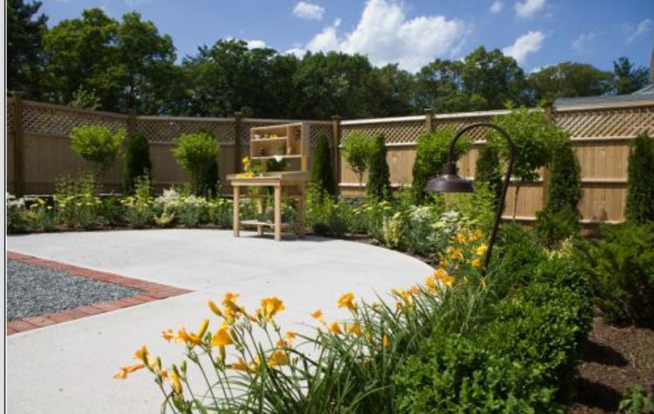 A beautifully landscaped garden featuring bright yellow daylilies and lush greenery, enclosed by a wooden fence.