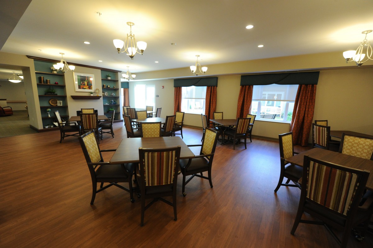 A cozy dining area with several tables and chairs, featuring wooden floors and warm lighting.