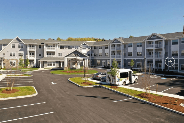 A modern apartment complex with a parking lot and a shuttle bus parked outside.