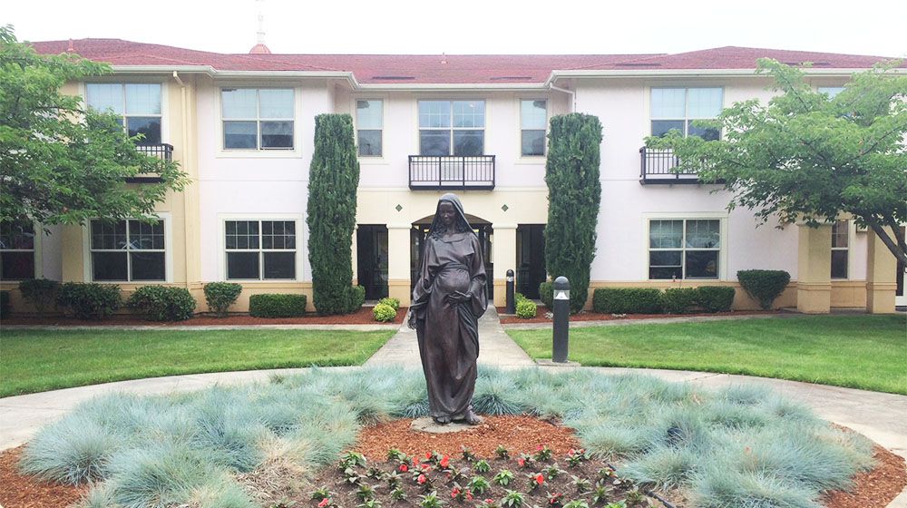 A statue in front of a two-story building with well-maintained gardens.