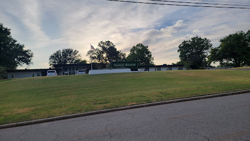 A serene view of a grassy area surrounded by trees under a partly cloudy sky.