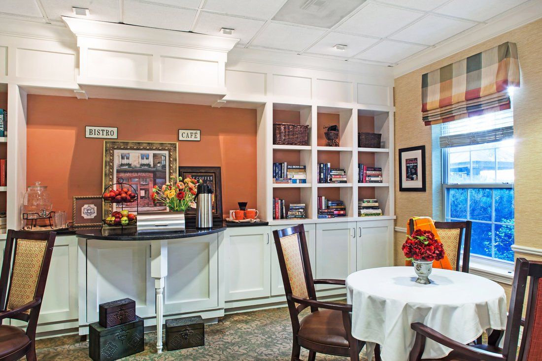 A well-decorated kitchen area with shelves, chairs, and a table adorned with flowers.