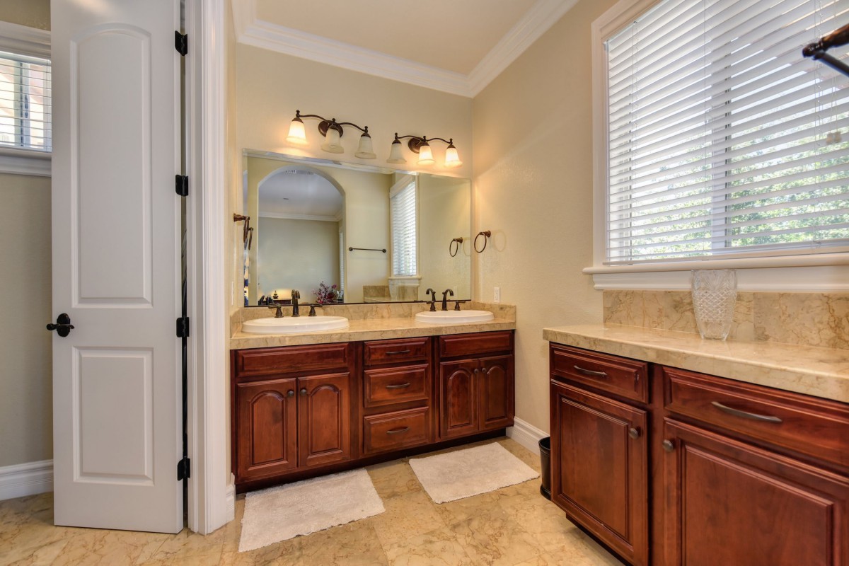 A well-designed bathroom featuring a double sink vanity with wooden cabinets, modern lighting, and tiled flooring.