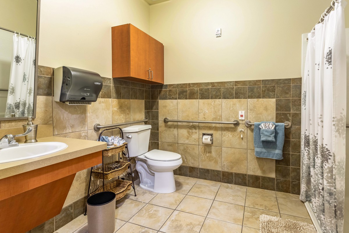 An accessible bathroom with a toilet, sink, handrails, and tiled flooring.