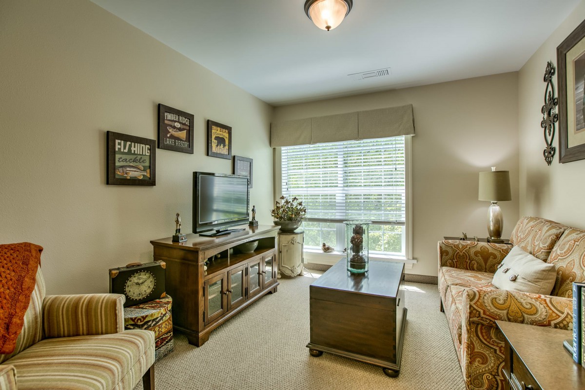 A cozy living room with a television, sofa, and coffee table, complemented by decorative artwork and a large window.