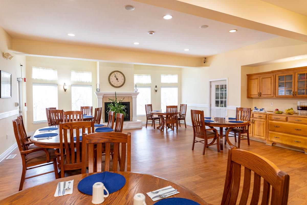 A spacious and well-lit dining room with wooden tables and chairs, decorated with a clock on the wall.