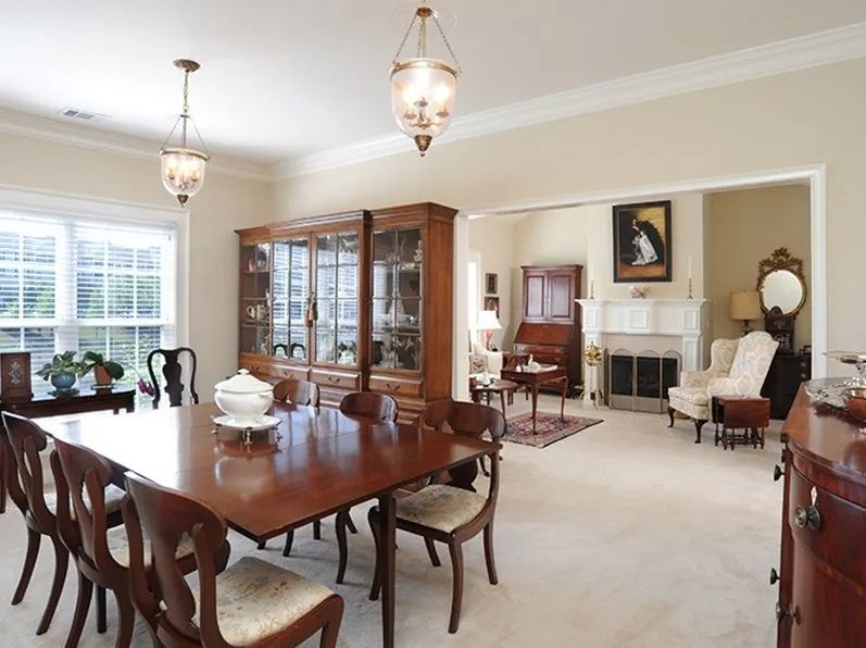 A traditional dining room with a wooden table, chairs, and a cabinet showcasing elegant decor.
