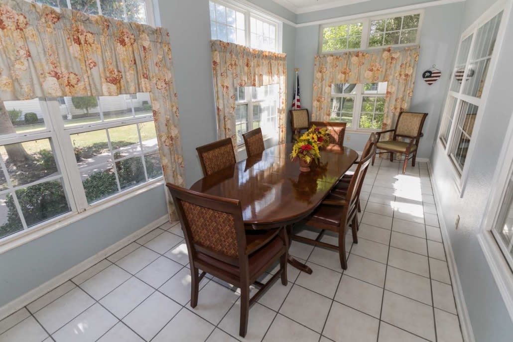 A bright dining room with a wooden table, chairs, and large windows adorned with patterned curtains.