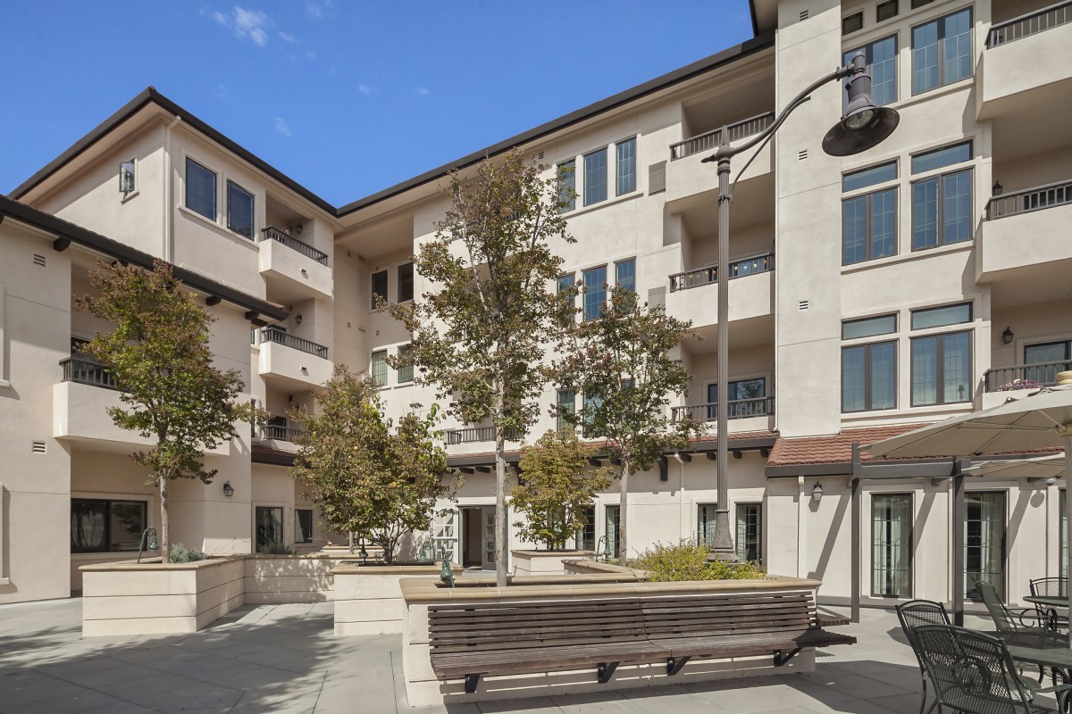 A modern apartment building with a landscaped courtyard featuring trees and benches.