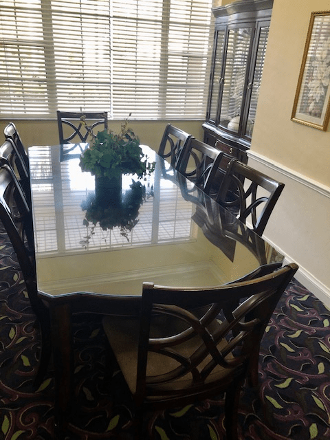 A dining room with a large table and eight chairs, featuring floral centerpiece decor and window blinds.