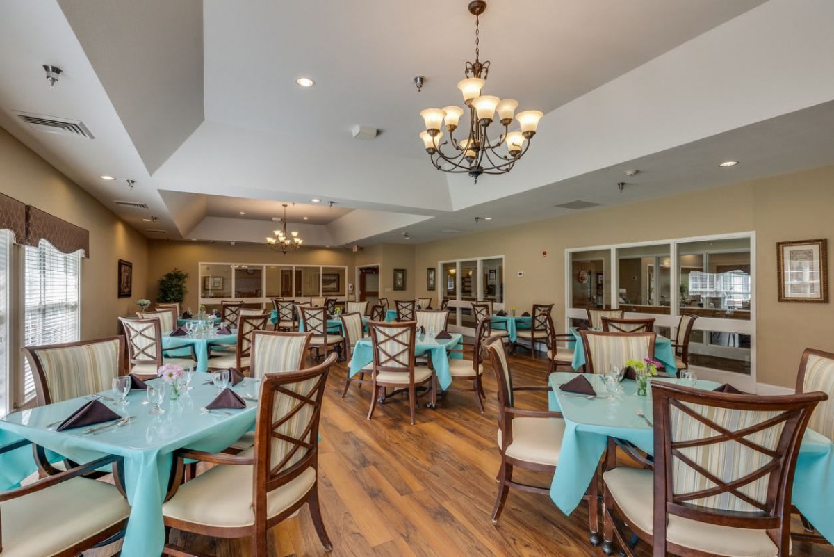 A spacious dining room with neatly arranged tables, turquoise tablecloths, and elegant chandeliers.