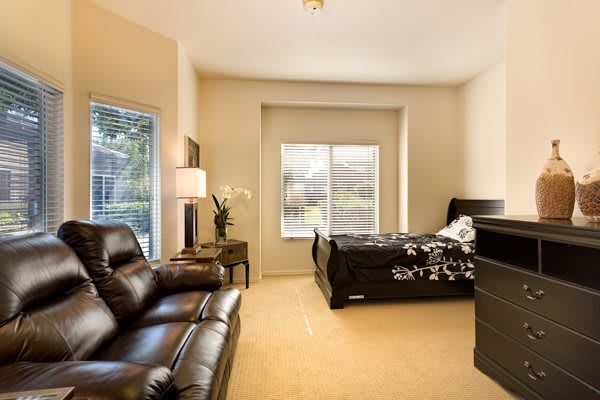 A cozy bedroom with a bed, leather sofa, and large window.