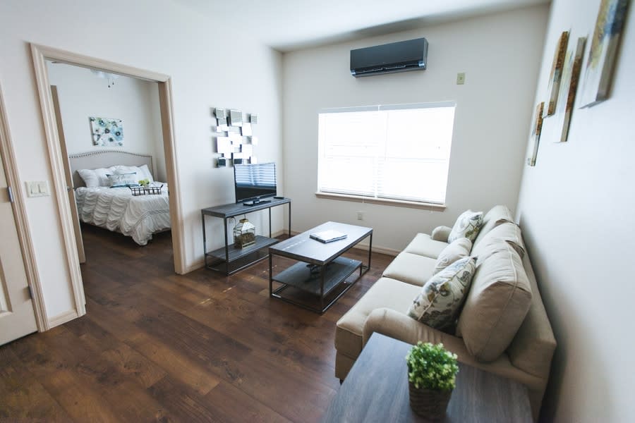 A modern living room with a cozy sofa, coffee table, and television, leading into a bedroom.