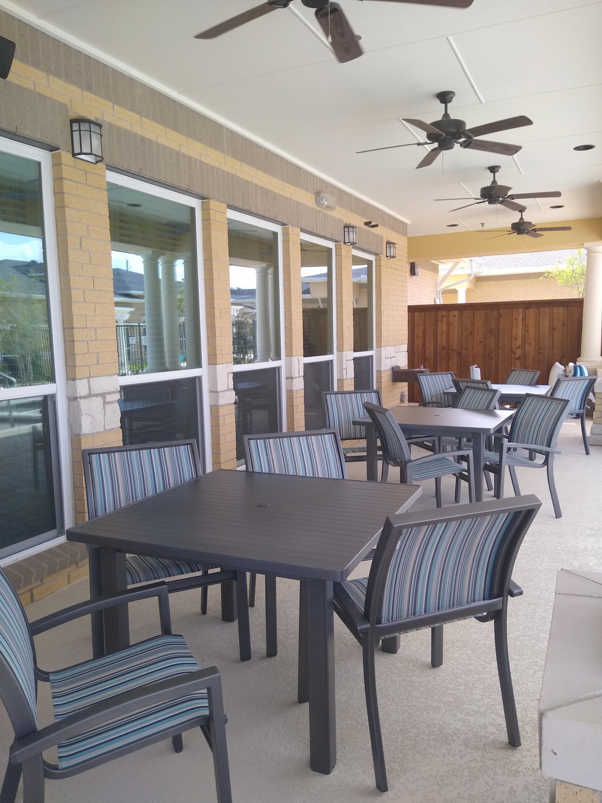 A covered outdoor patio with tables and chairs, featuring ceiling fans for comfort.