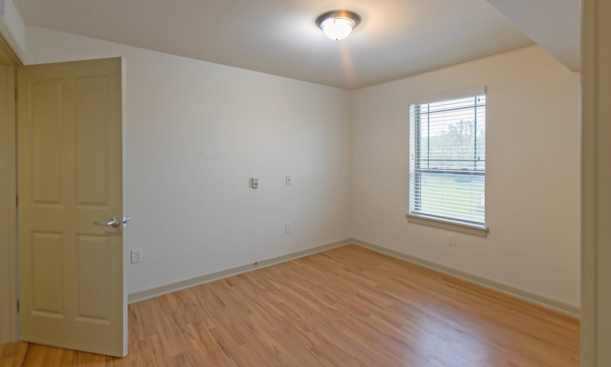 An empty room with hardwood flooring and a window letting in natural light.
