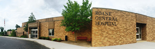 Exterior view of a brick hospital building with a tree and bench.