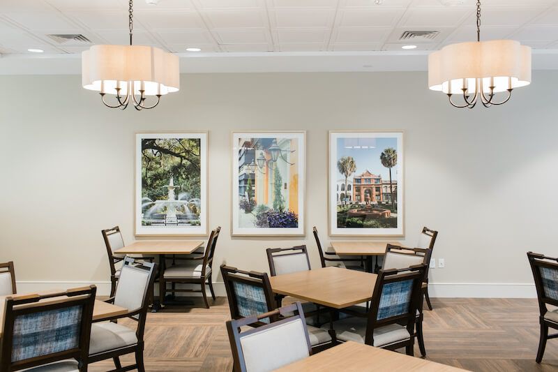 A modern dining area with tables and chairs, featuring artwork on the walls and elegant lighting fixtures.