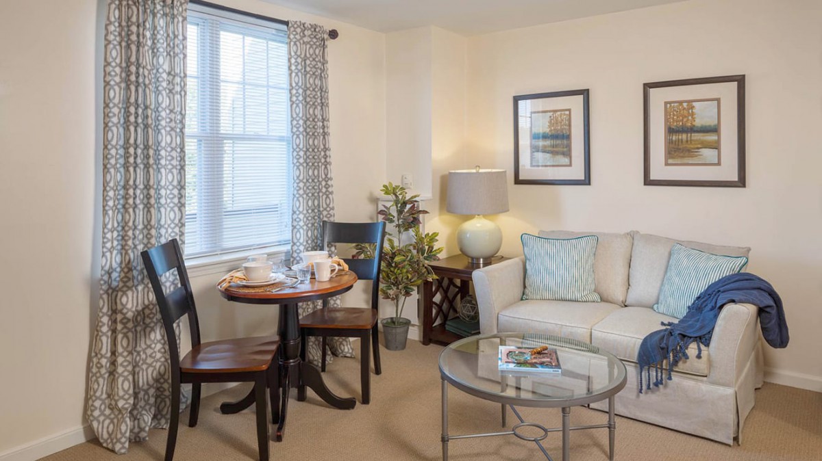 A cozy living room with a sofa, coffee table, and a dining area by the window.