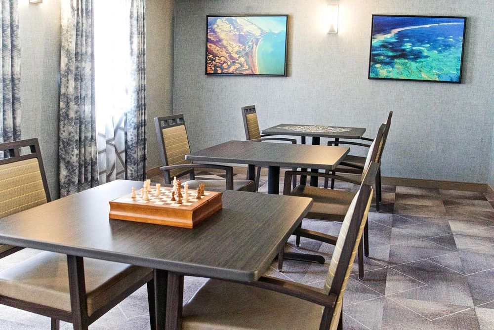 A cozy room with several tables and chairs, featuring a chessboard and wall artwork.