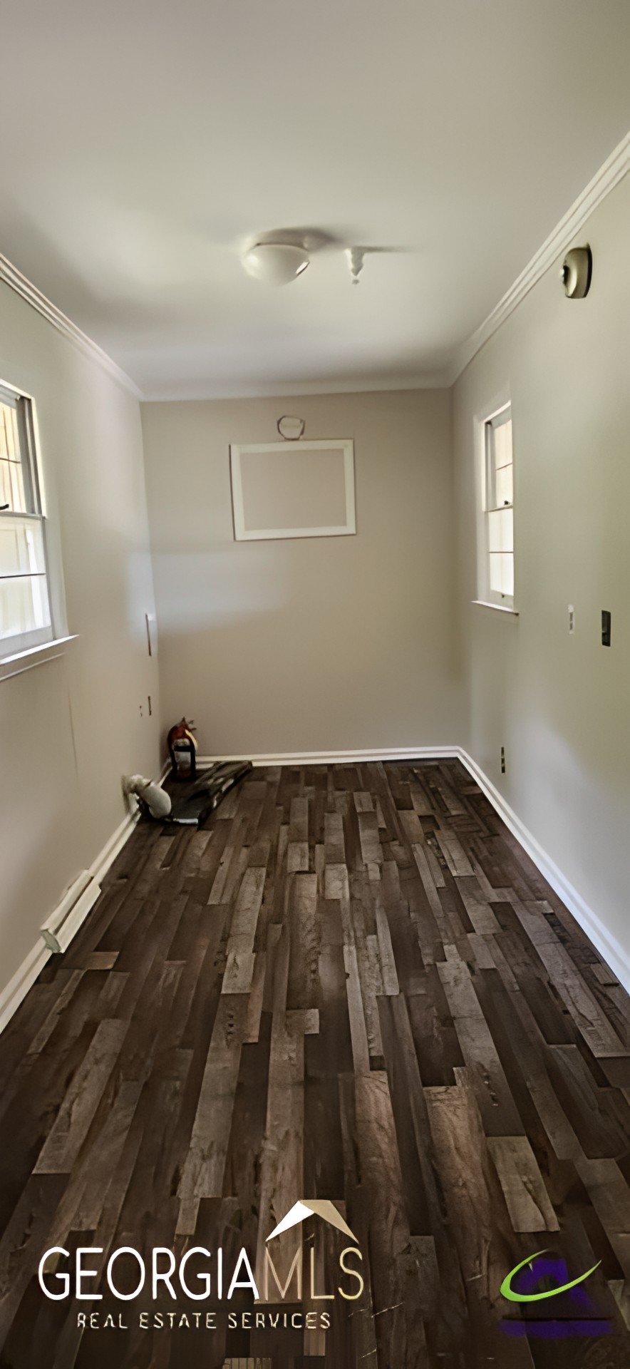 An empty room with wooden flooring and two windows.