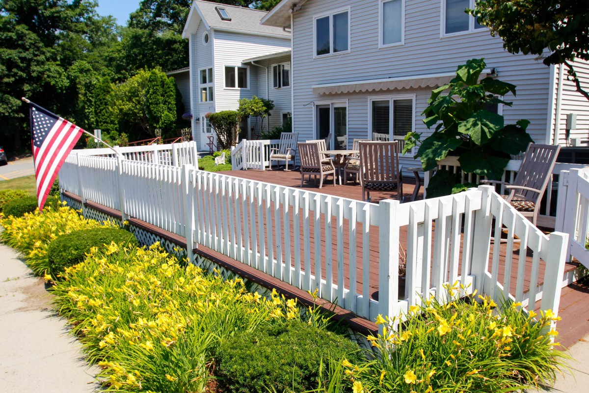 A charming backyard deck with white fencing, surrounded by a blooming garden and outdoor seating area.