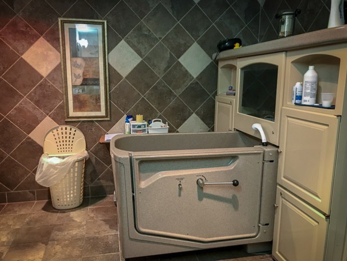 A bathroom featuring a large walk-in bathtub and tiled walls, with a mirror and storage cabinet.